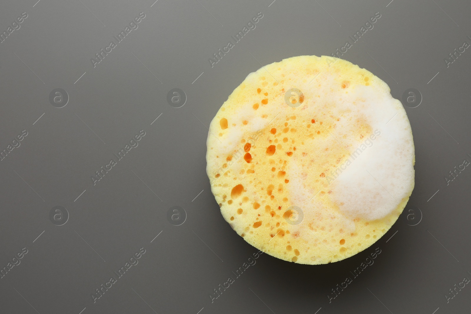 Photo of Yellow sponge with foam on grey background, top view. Space for text