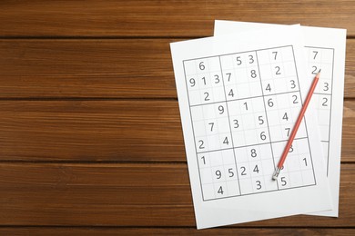 Photo of Sudoku and pencil on wooden table, top view. Space for text