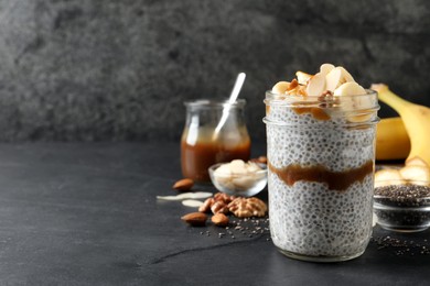 Photo of Delicious chia pudding with banana, walnuts and caramel sauce on black table, space for text