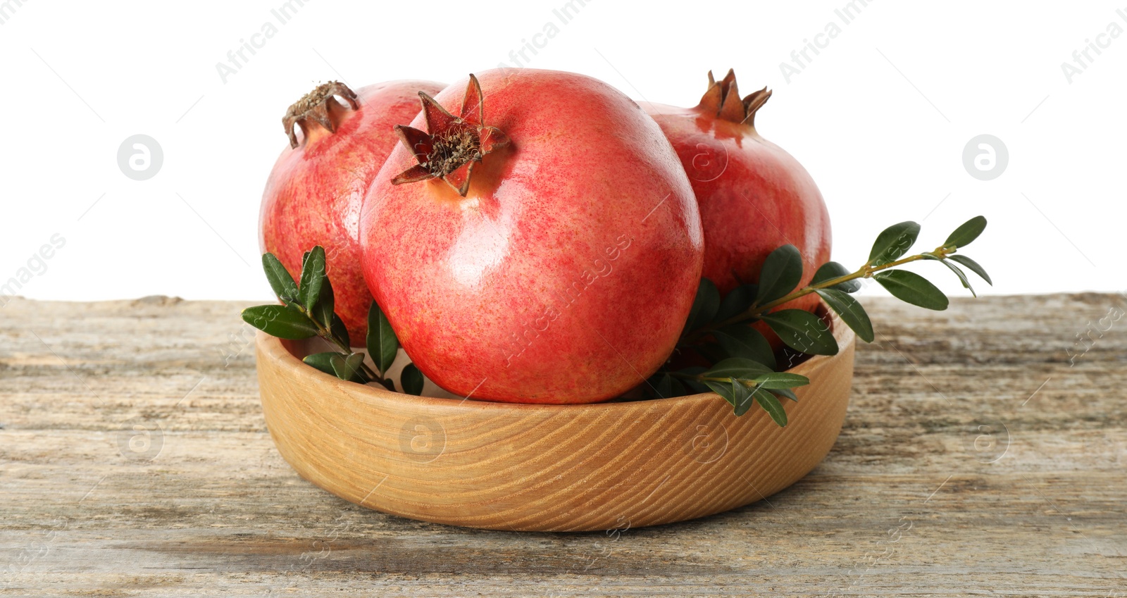 Photo of Fresh pomegranates and green leaves in bowl on wooden table against white background