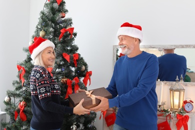 Mature couple in Santa hats with Christmas gift box at home