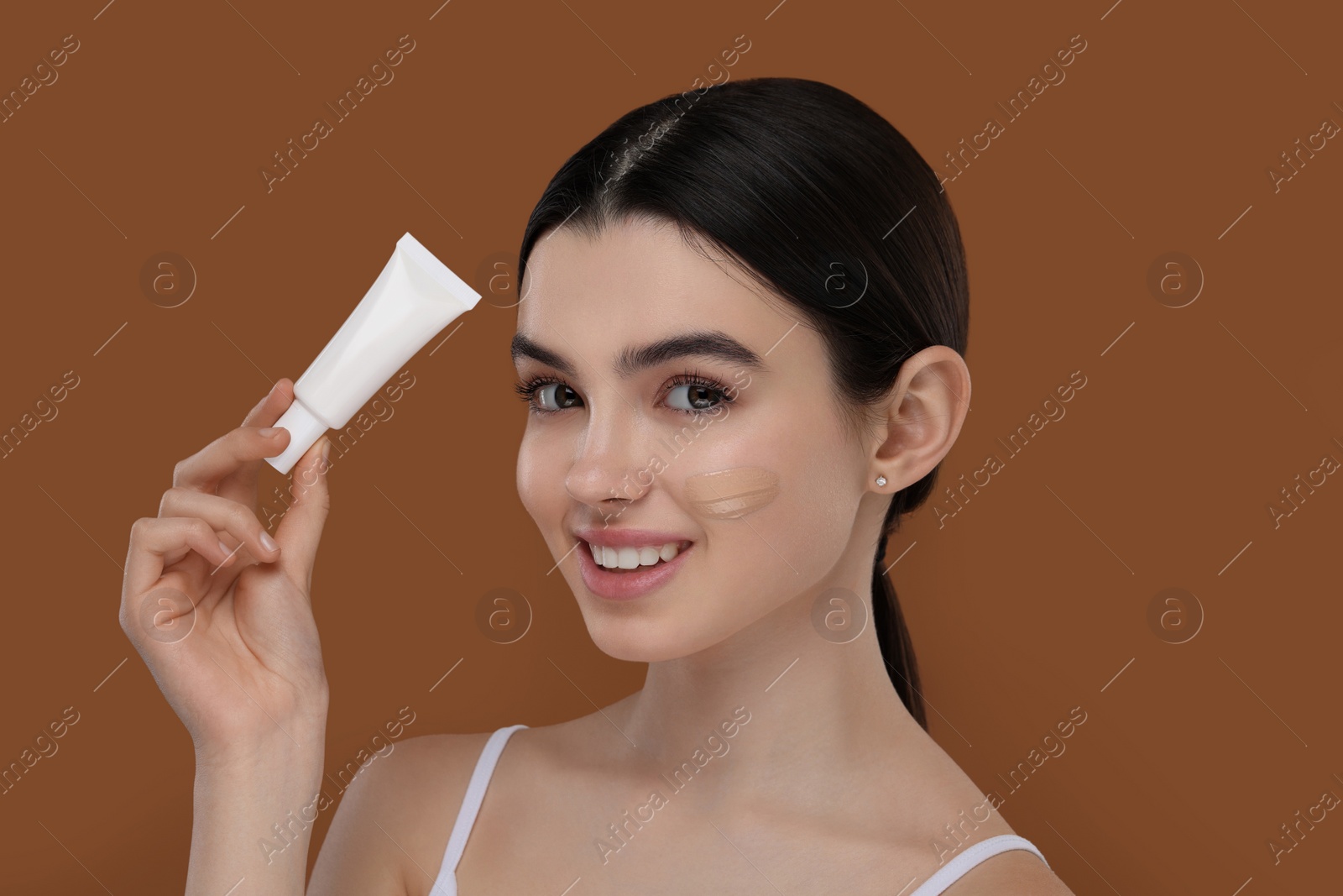 Photo of Teenage girl holding tube with foundation on brown background