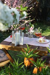 Photo of Vase with spring flowers, wine and cake on table served for romantic date in garden