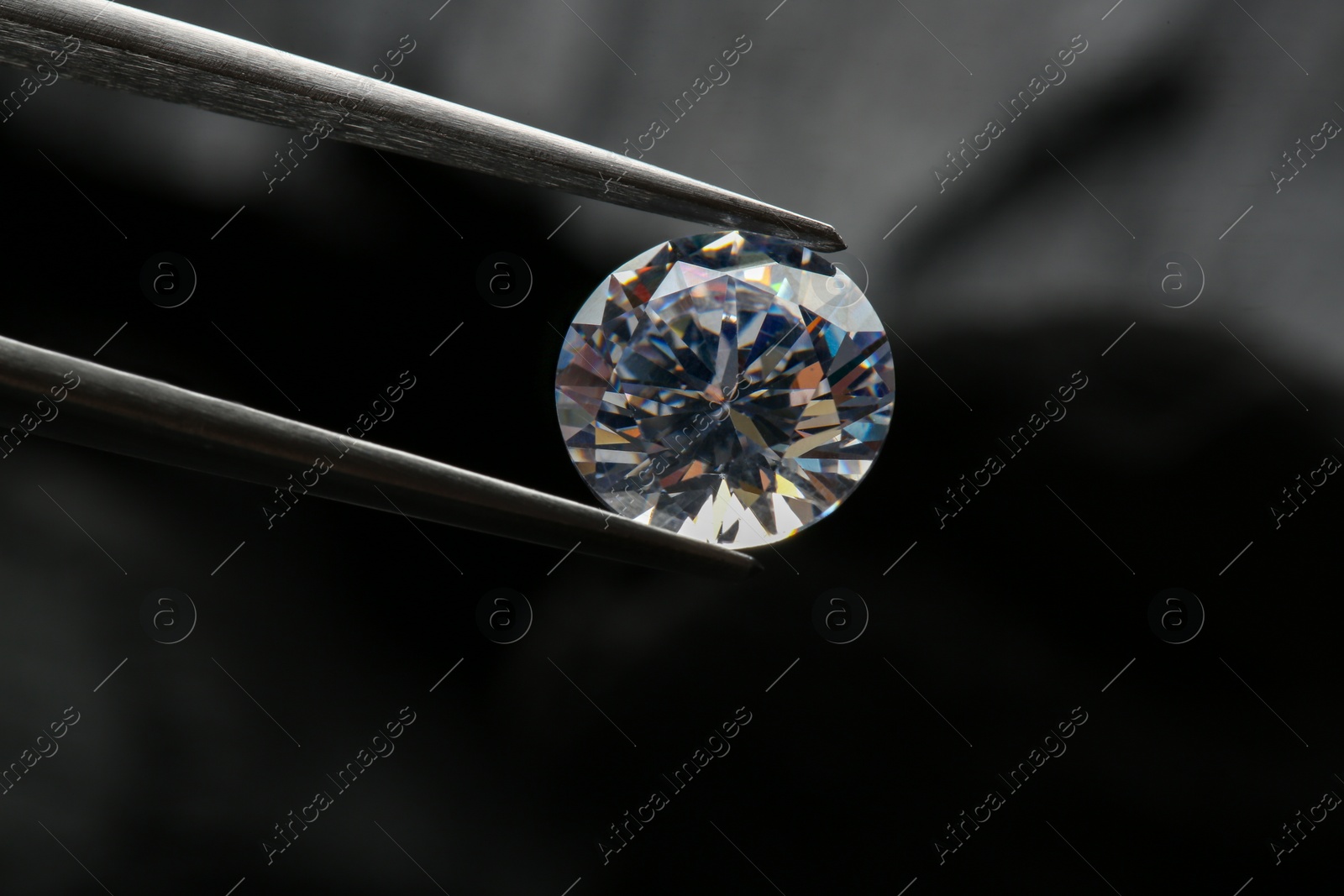 Photo of Tweezers with beautiful shiny diamond on dark background, closeup