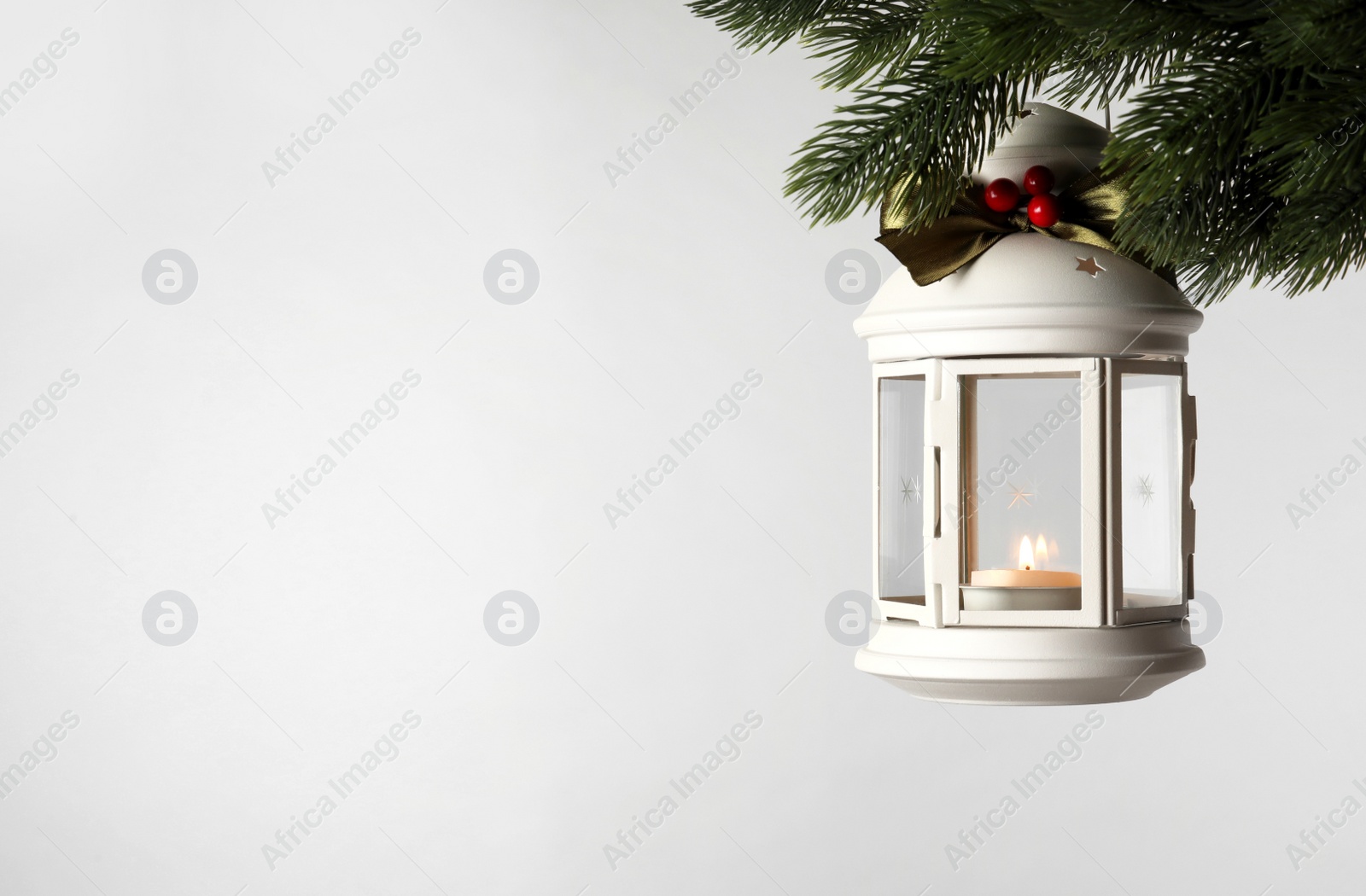 Photo of Vintage Christmas lantern with burning candle hanging on fir branch against light background. Space for text