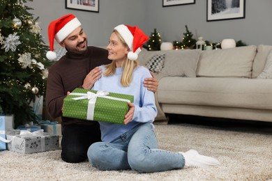 Happy couple in Santa hats with Christmas gift at home