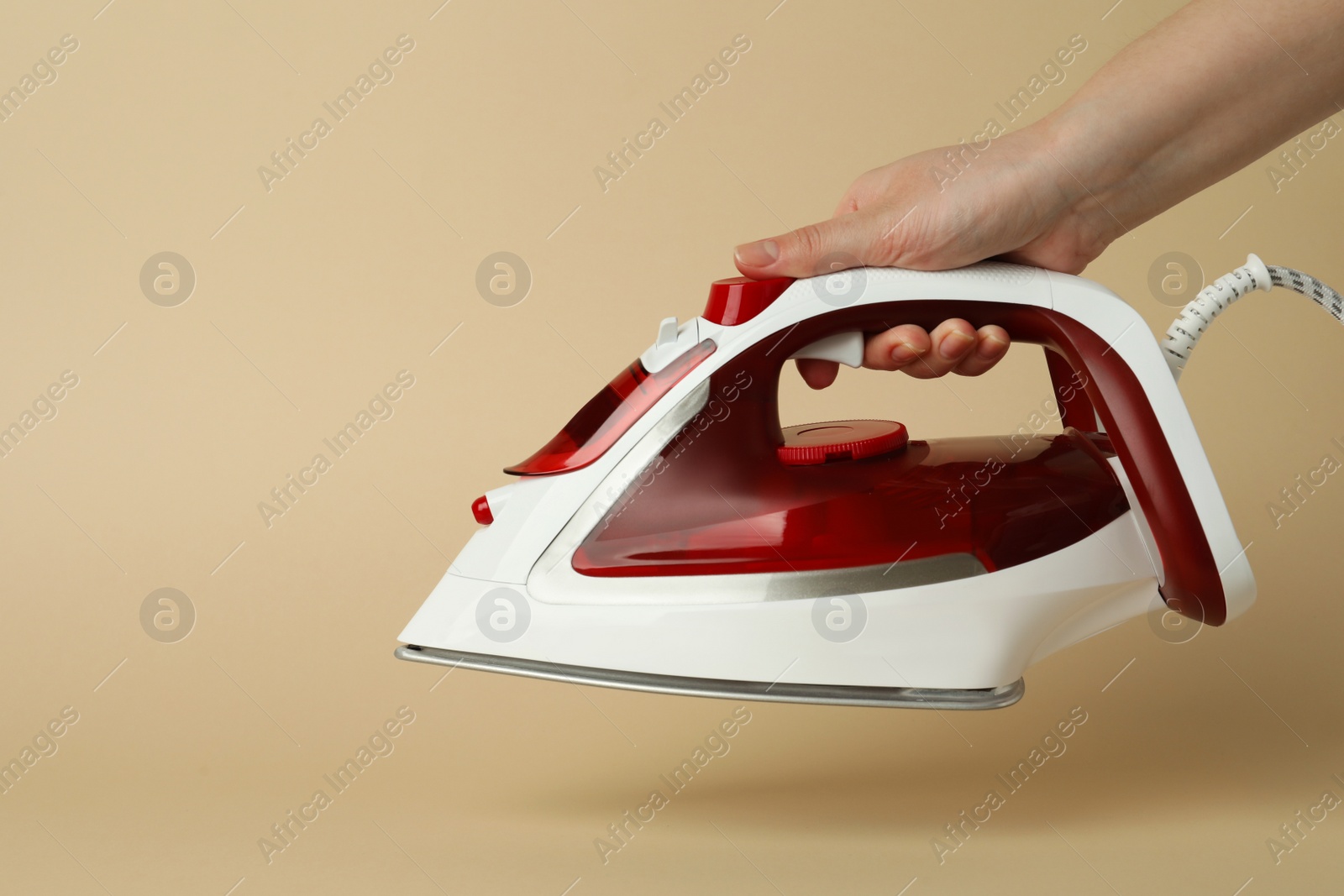 Photo of Woman holding modern iron on beige background, closeup