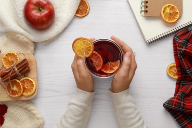 Woman holding cup of hot tea at white wooden table, top view. Cozy winter