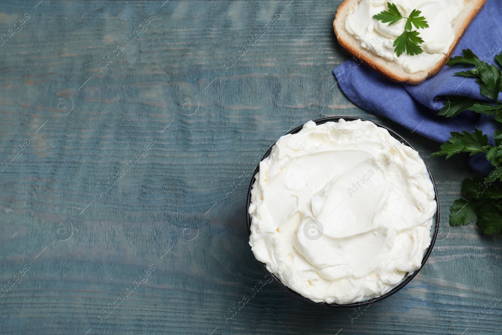 Photo of Tasty cream cheese, fresh bread and parsley on light blue wooden table, flat lay. Space for text