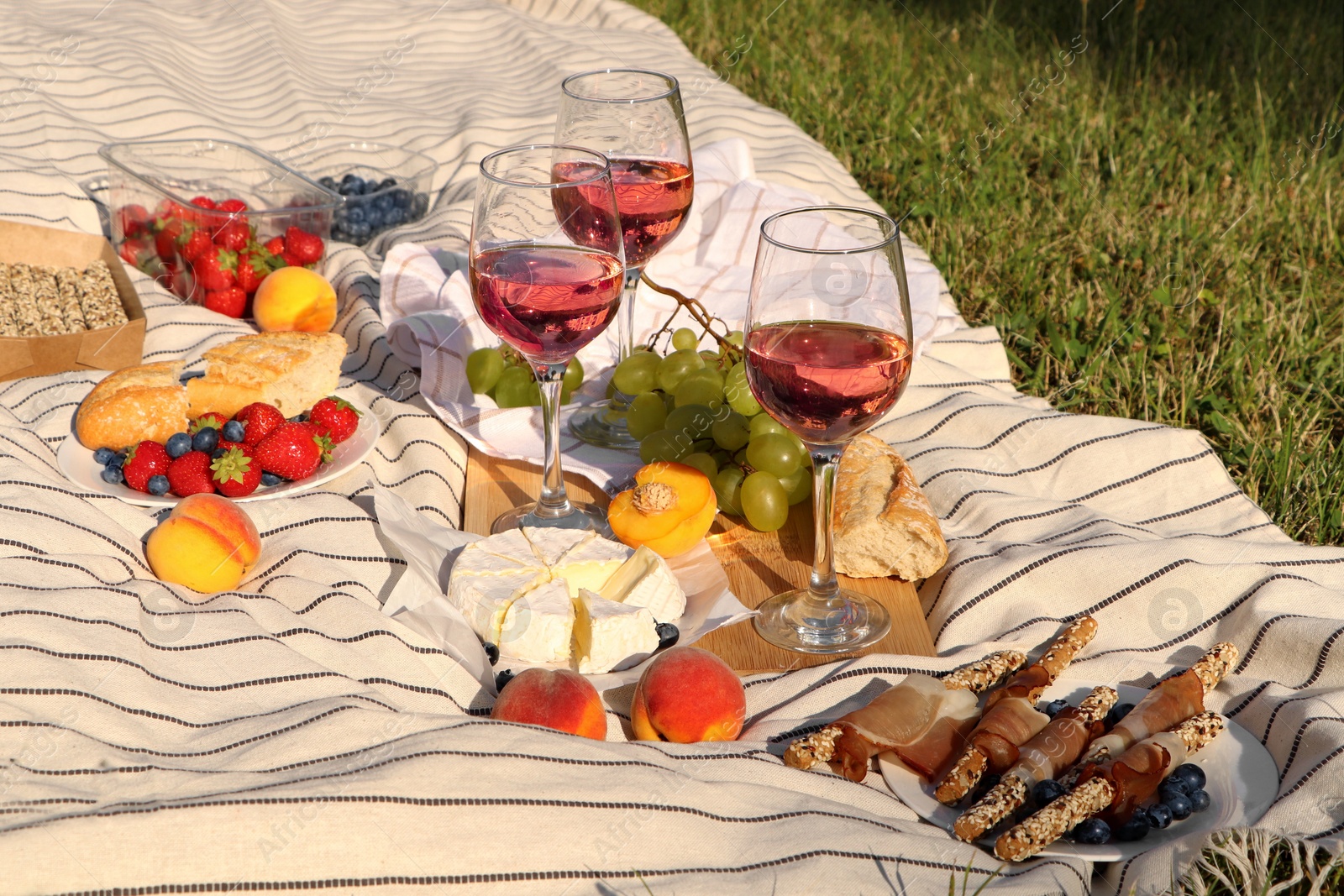 Photo of Glasses of delicious rose wine and food on picnic blanket outdoors