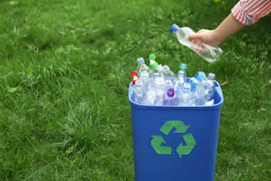 Photo of Woman throwing used bottle into trash bin outdoors, closeup. Plastic recycling