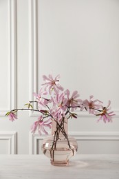 Photo of Magnolia tree branches with beautiful flowers in glass vase on white wooden table