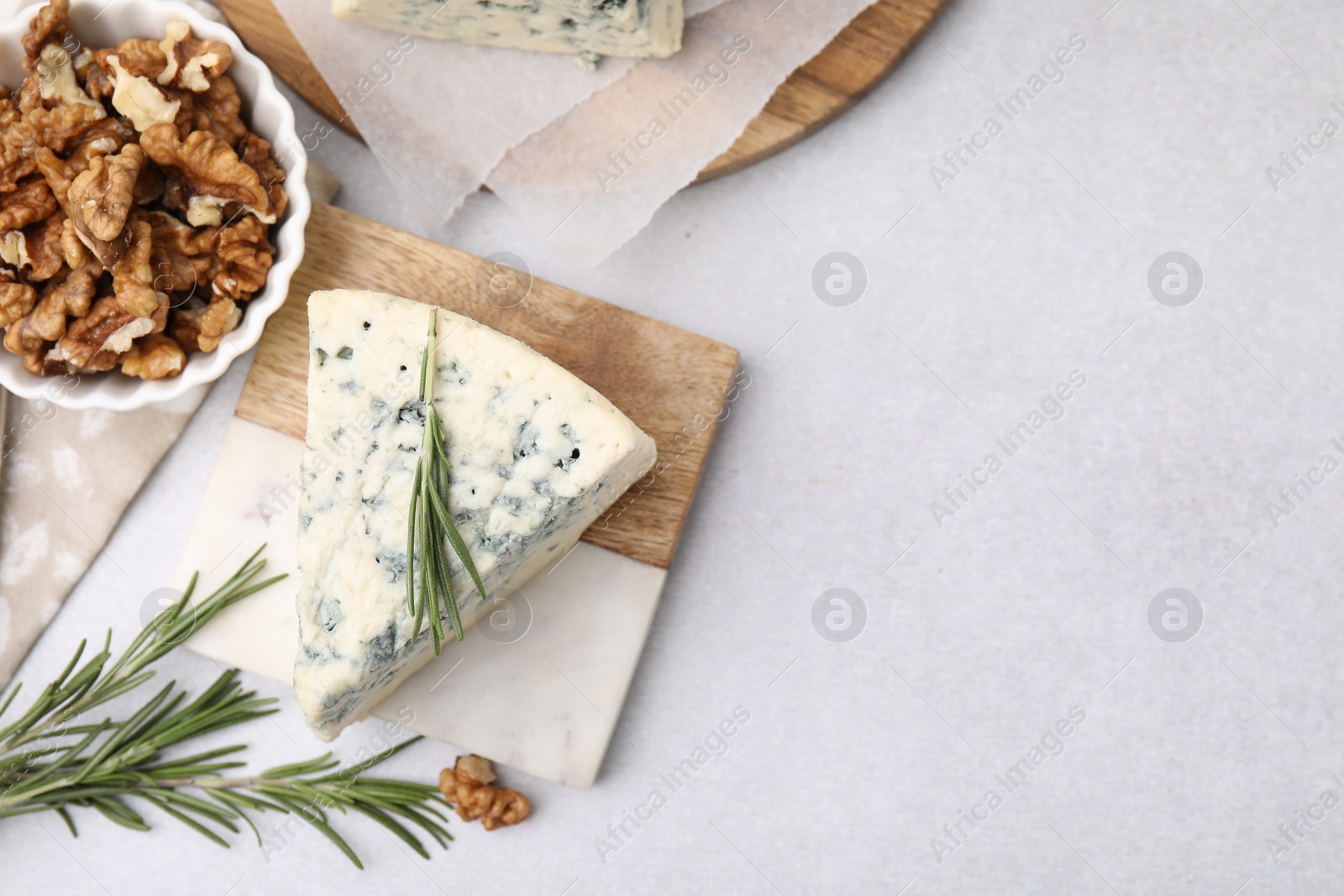 Photo of Tasty blue cheese with rosemary and walnuts on light table, flat lay. Space for text