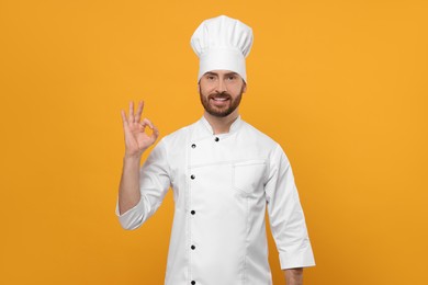Photo of Smiling mature chef showing ok gesture on orange background