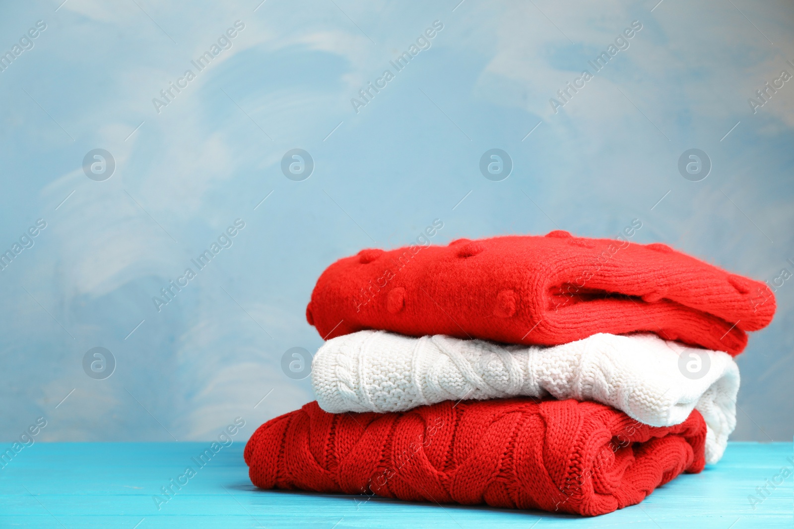 Photo of Stack of folded knitted sweaters on table. Space for text