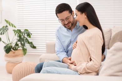 Photo of Happy pregnant woman spending time with her husband on sofa at home