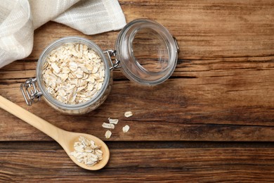 Photo of Raw oatmeal, spoon and glass jar on wooden table, flat lay. Space for text