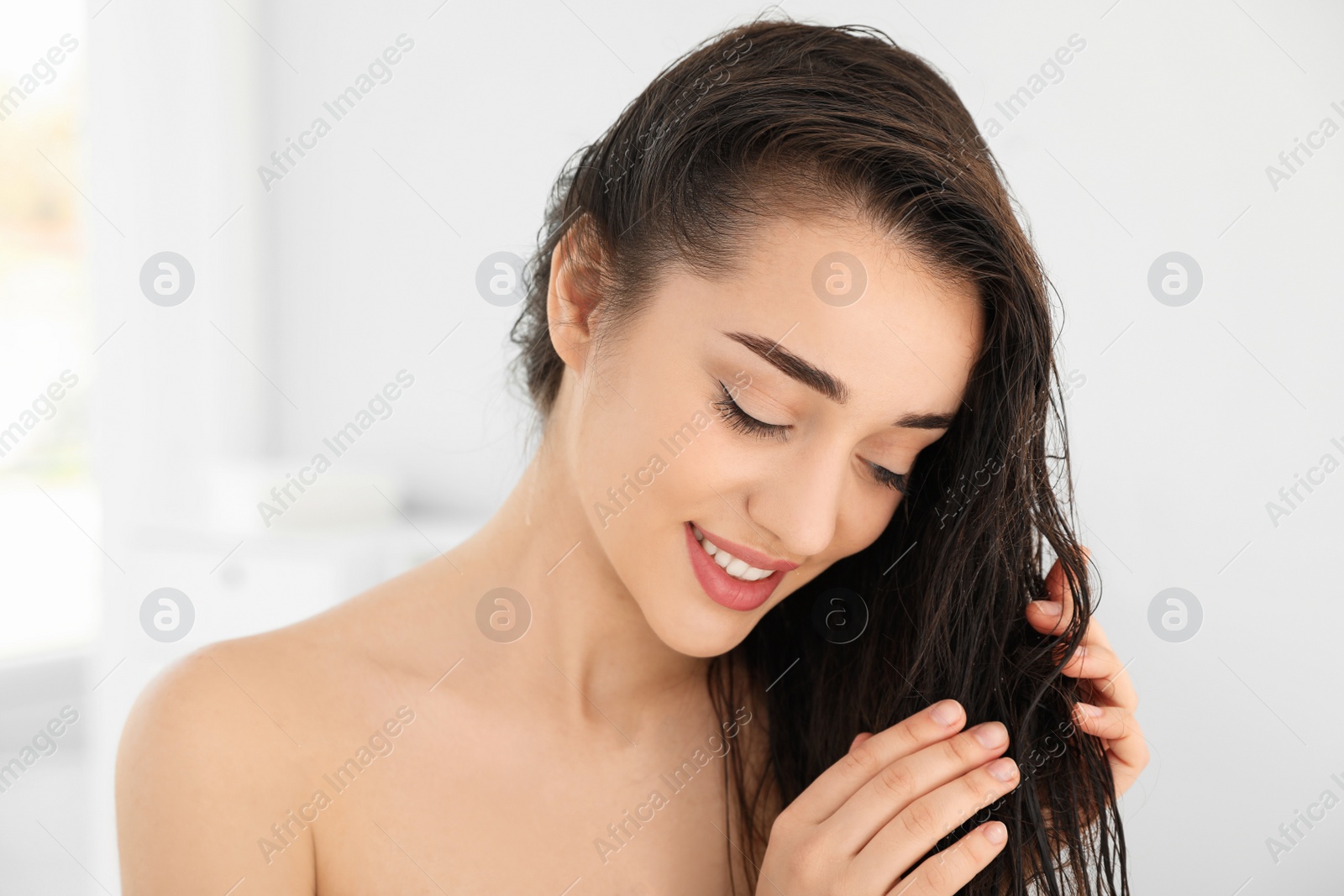 Photo of Beautiful young woman applying hair conditioner in bathroom