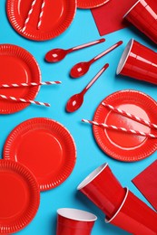 Disposable tableware on light blue background, flat lay