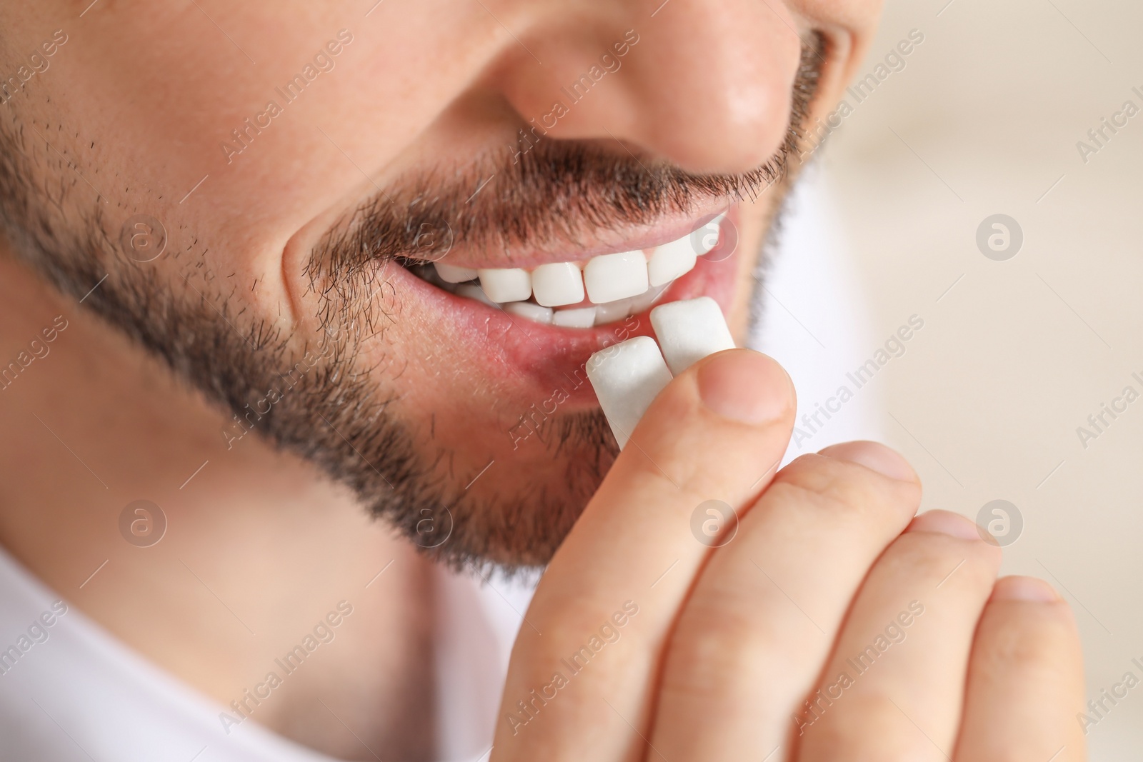 Photo of Man putting chewing gums into mouth on blurred background, closeup