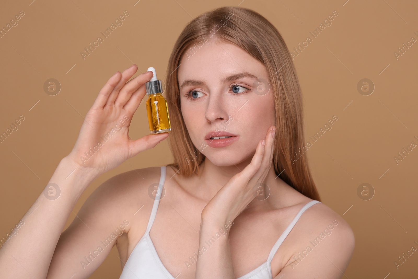 Photo of Beautiful young woman with bottle of essential oil on brown background