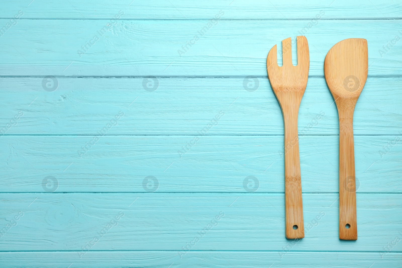 Photo of Wooden spatula and fork on color background, top view with space for text