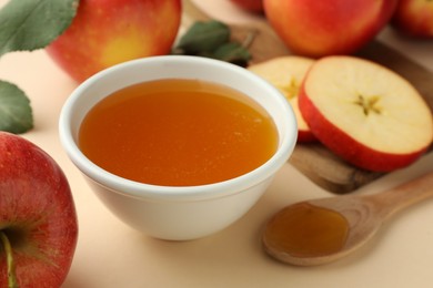 Photo of Delicious apples, bowl of honey and spoon on beige background, closeup