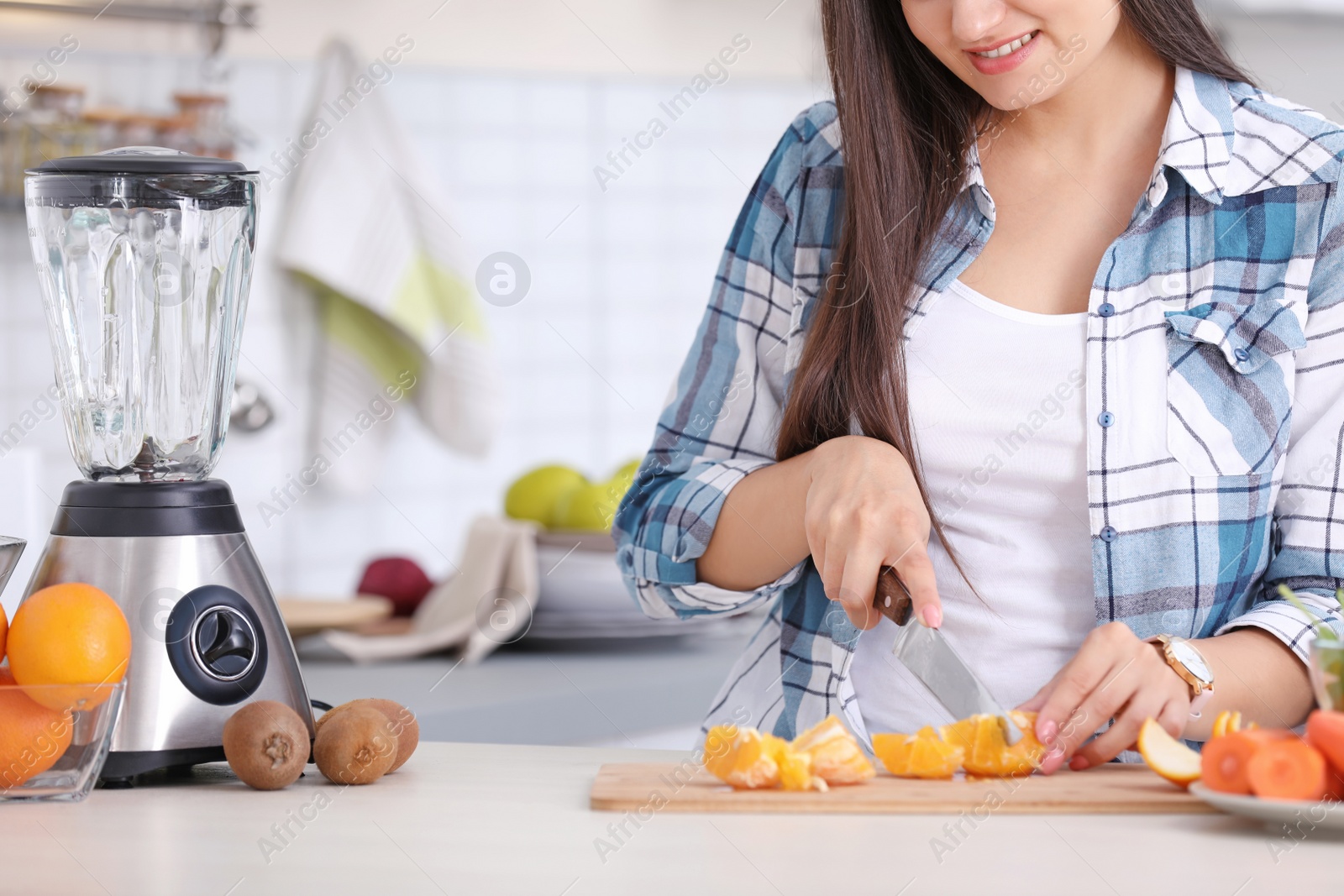 Photo of Young woman preparing tasty healthy smoothie at table in kitchen