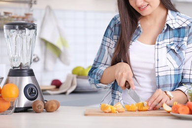 Young woman preparing tasty healthy smoothie at table in kitchen