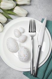Festive table setting with painted eggs and cutlery on light grey background, flat lay. Easter celebration