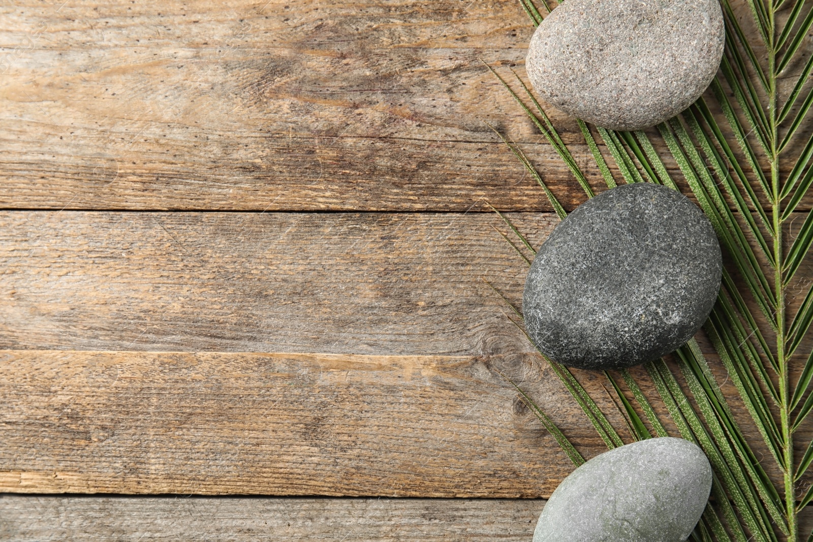 Photo of Zen stones and tropical leaf on wooden background, top view with space for text