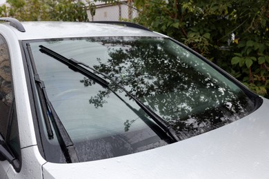 Wipers cleaning raindrops from car windshield outdoors