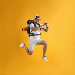 Photo of Male tourist with travel backpack taking picture on yellow background