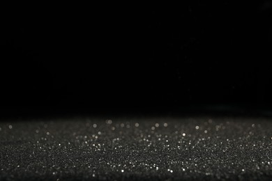 Shiny grey glitter on black background, space for text. Bokeh effect