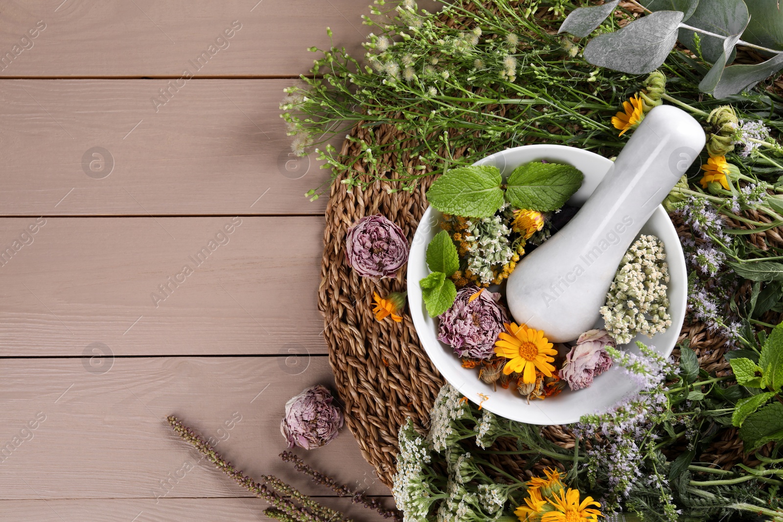 Photo of Mortar with pestle and many different herbs on wooden table, flat lay. Space for text