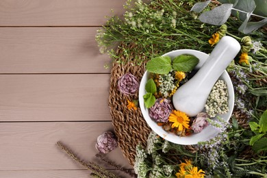 Mortar with pestle and many different herbs on wooden table, flat lay. Space for text