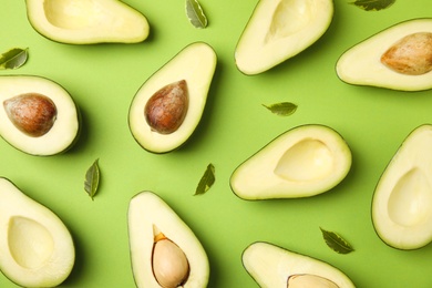 Cut fresh ripe avocados and leaves on green background, flat lay