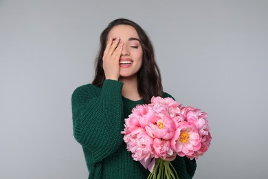 Beautiful young woman with bouquet of peonies on light grey background