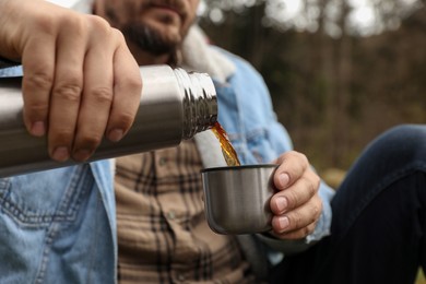 Photo of Man pouring hot drink from metallic thermos into cup lid outdoors, closeup