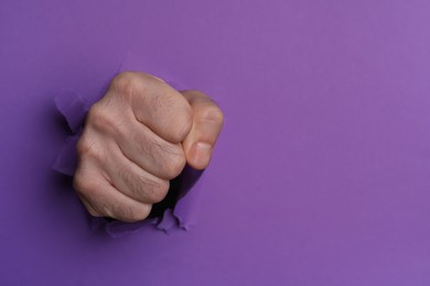 Photo of Man breaking through purple paper with fist, closeup. Space for text
