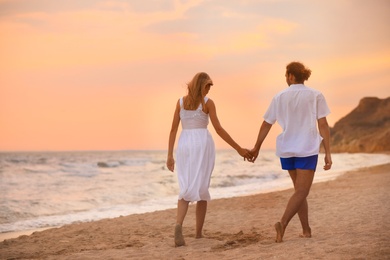 Photo of Young couple walking on beach at sunset