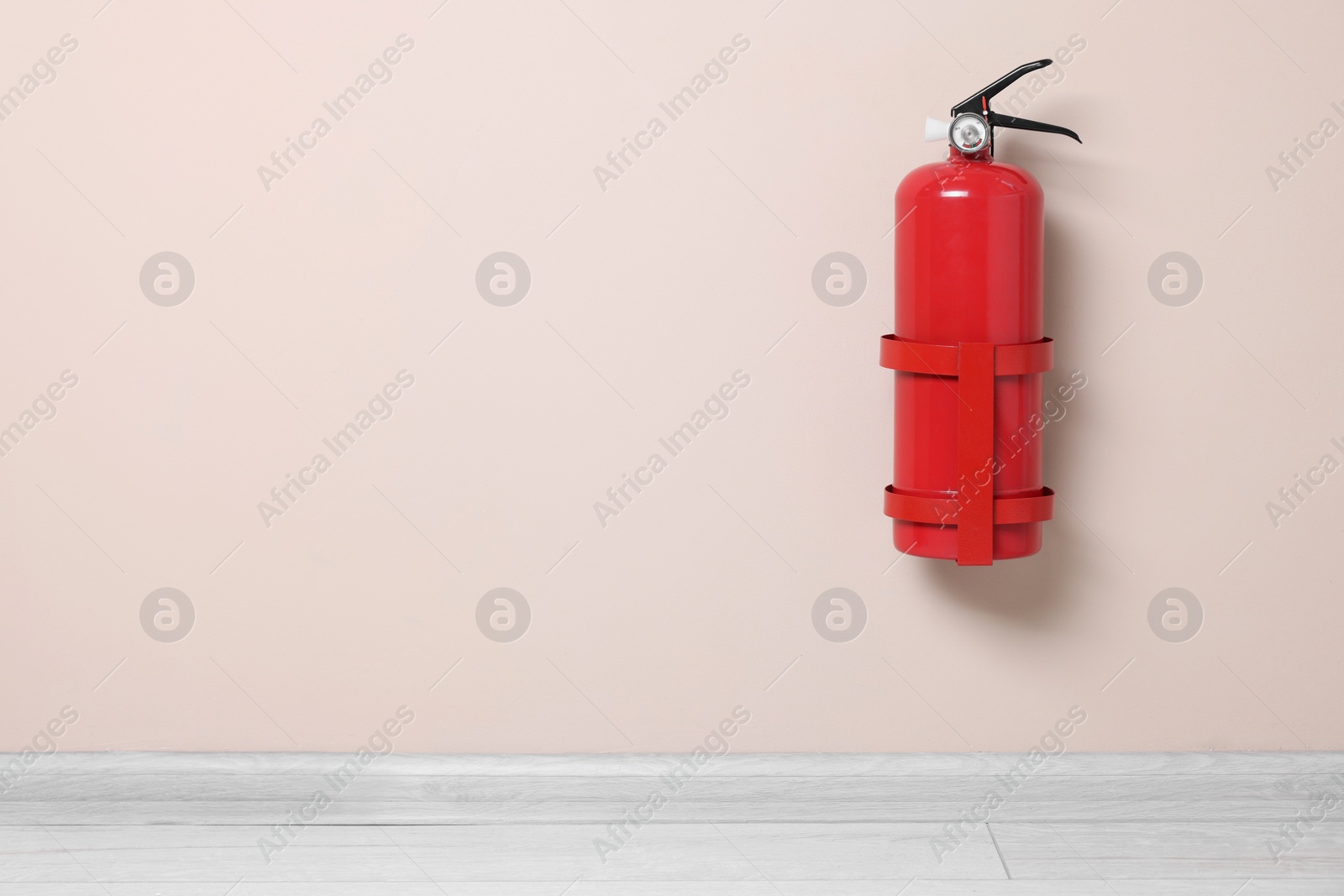 Photo of One fire extinguisher on beige wall, space for text