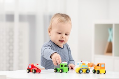 Children toys. Cute little boy playing with toy cars at white table in room