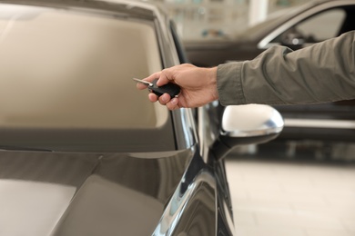 Photo of Young man checking alarm system with car key indoors, closeup