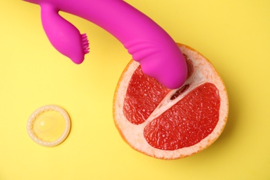 Photo of Half of grapefruit, purple vibrator and condom on yellow background, flat lay. Sex concept