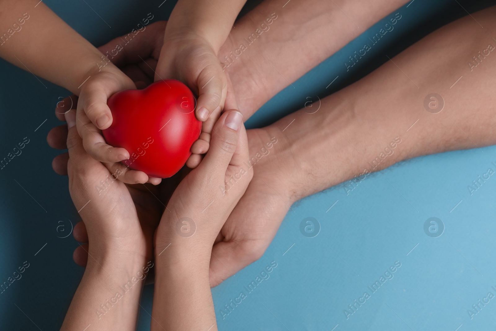 Photo of Parents and child holding red decorative heart on light blue background, top view