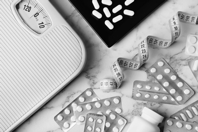 Photo of Flat lay composition with weight loss pills, scales and measuring tape on marble background