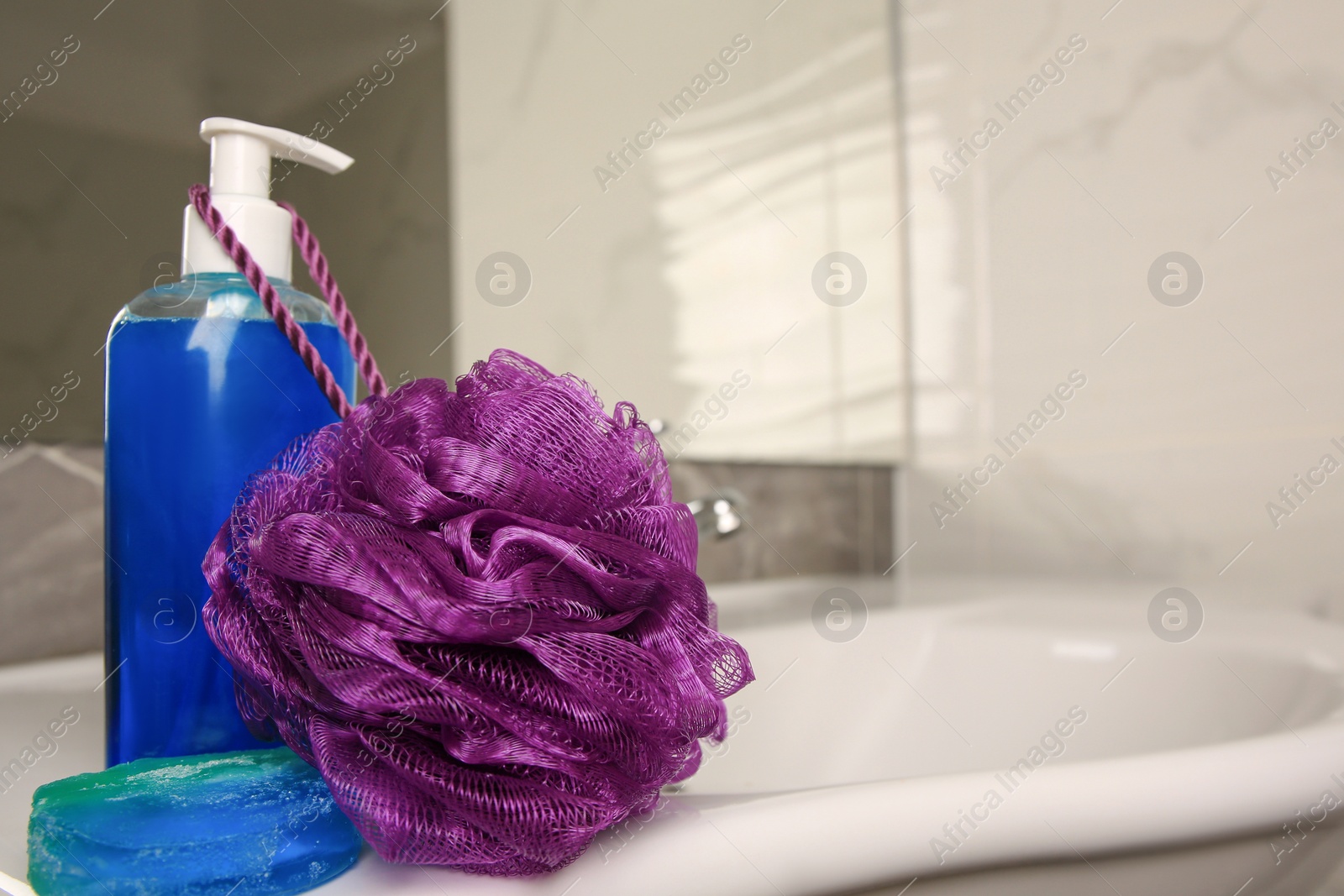 Photo of Purple shower puff and cosmetic products on sink in bathroom, space for text