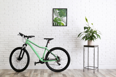 Photo of Modern green bicycle near white brick wall in stylish room interior