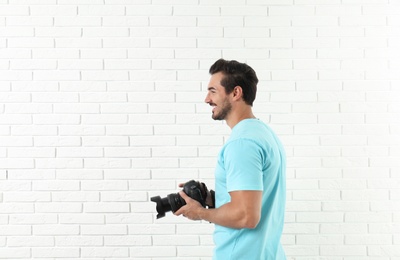 Young photographer with professional camera near brick wall. Space for text